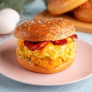 Sesame hamburger bun filled with pieces of bacon, melted cheese, scrambled egg and a hash brown.