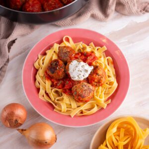 Plate of pasta with meatballs, tomato sauce, and ricotta on top.